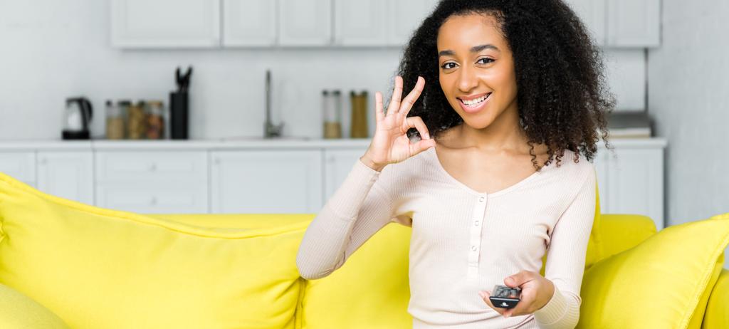heureuse femme afro-américaine avec télécommande à la main montrant ok signe
 - Photo, image
