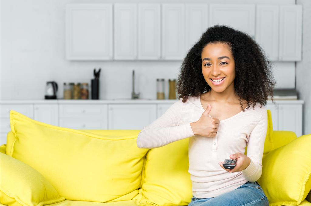heureuse femme afro-américaine avec télécommande à la main montrant pouce vers le haut
 - Photo, image