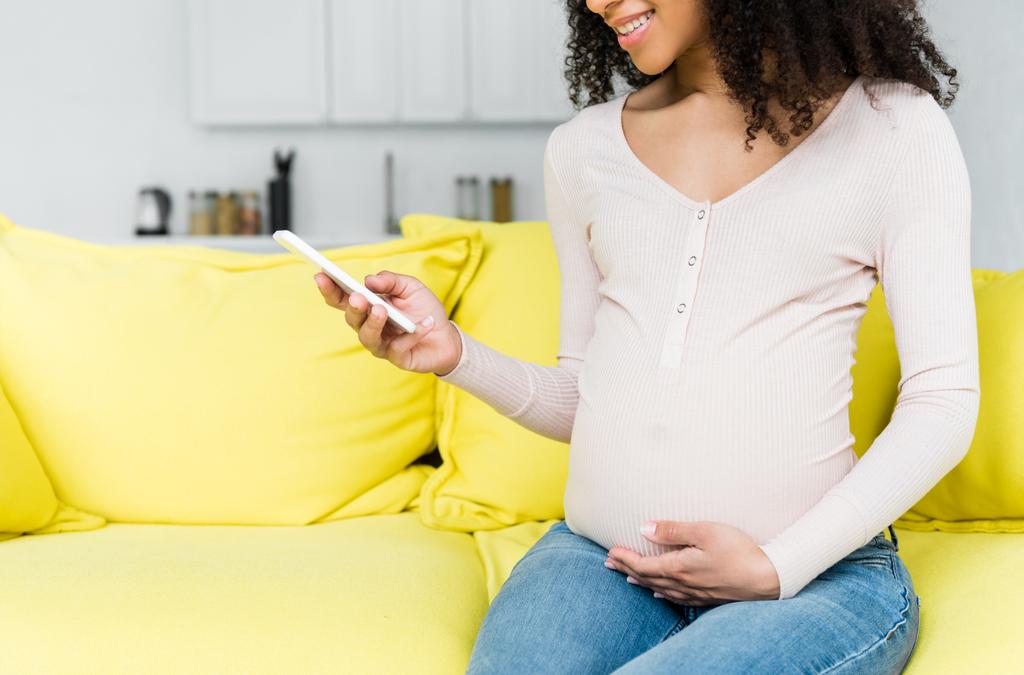 abgeschnittene Ansicht einer schwangeren Afroamerikanerin mittels Smartphone - Foto, Bild
