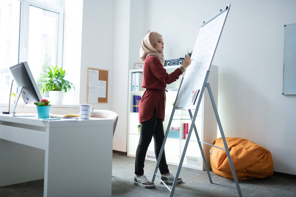 Μουσουλμάνος δάσκαλος στέκεται κοντά στον πίνακα και γράφοντας σημειώσεις - Φωτογραφία, εικόνα