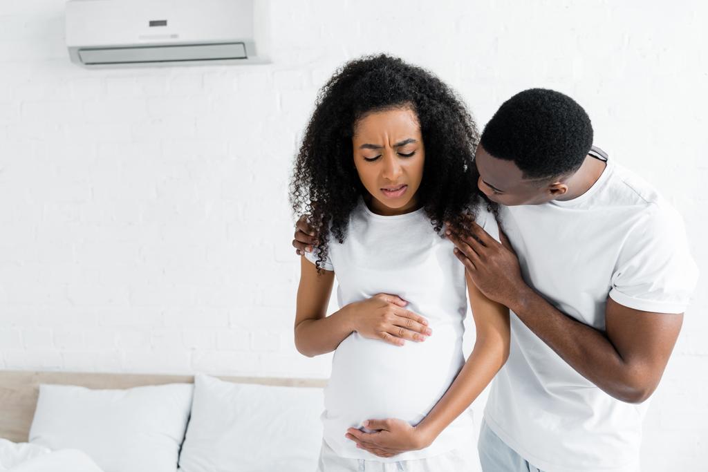 アフリカ系アメリカ人男性が心配して妊娠中の妻を部屋に抱きしめる - 写真・画像