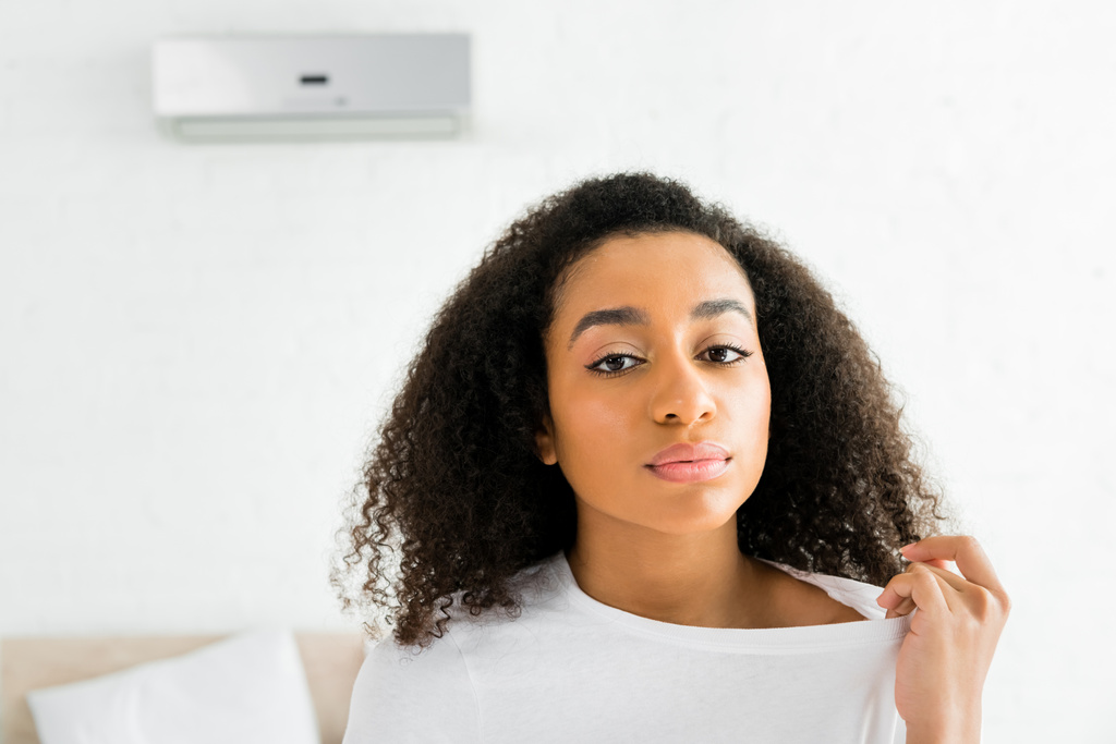 Porträt einer aufgebrachten afrikanisch-amerikanischen Frau, die auf einem Zimmer mit Klimaanlage steht und in die Kamera schaut - Foto, Bild