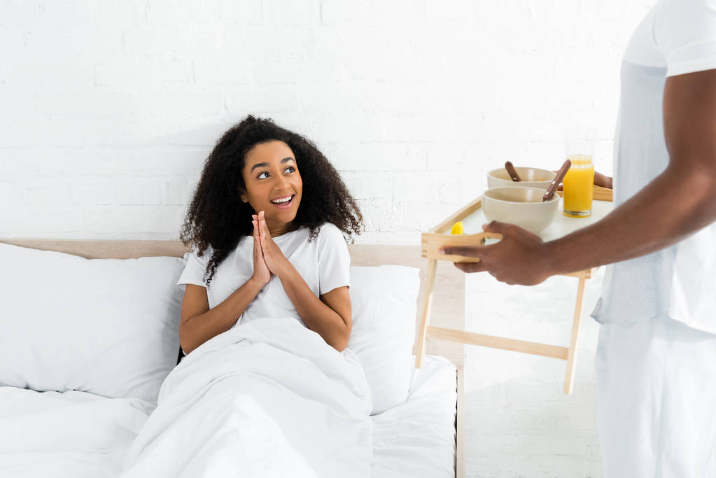 Africano americano mulher olhando para namorado com bandeja de café da manhã em mãos
 - Foto, Imagem