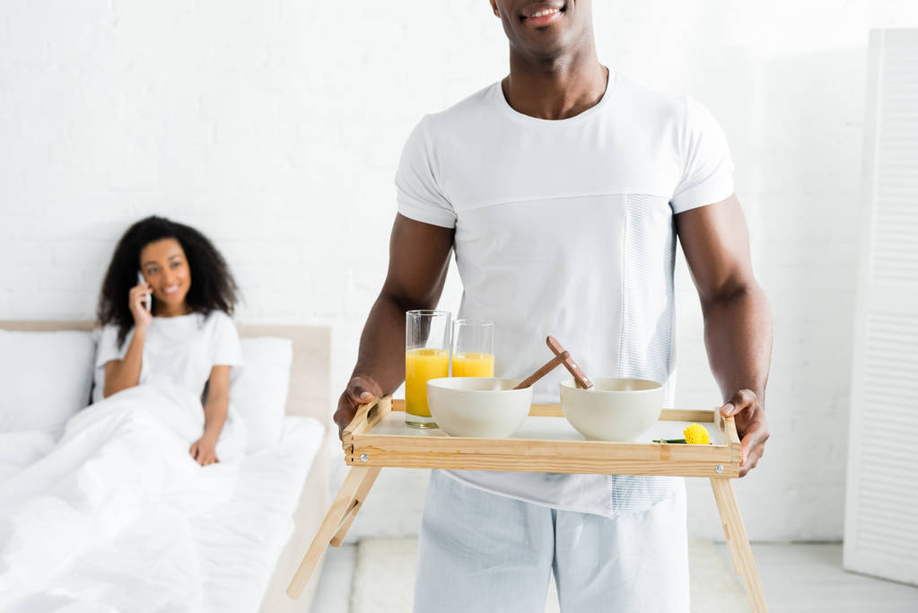 selektivní pohled na afroamerického muže držící v ruce snídani, s usměvavou přítelkyní na pozadí - Fotografie, Obrázek
