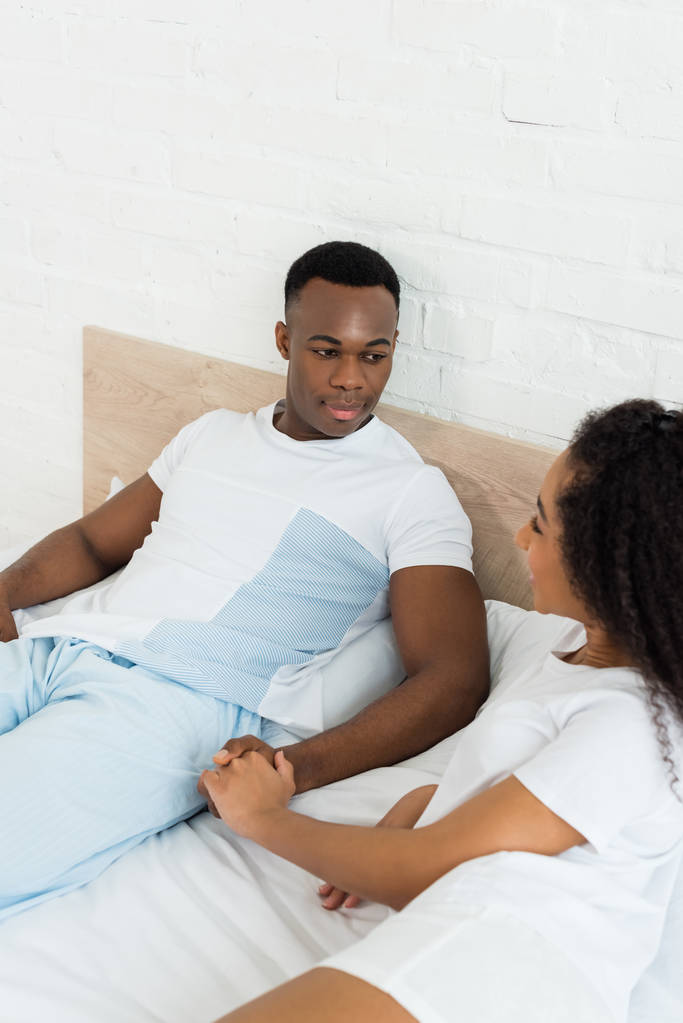 високий кут зору афроамериканця тримає руки з чарівною подругою, лежить на ліжку
 - Фото, зображення