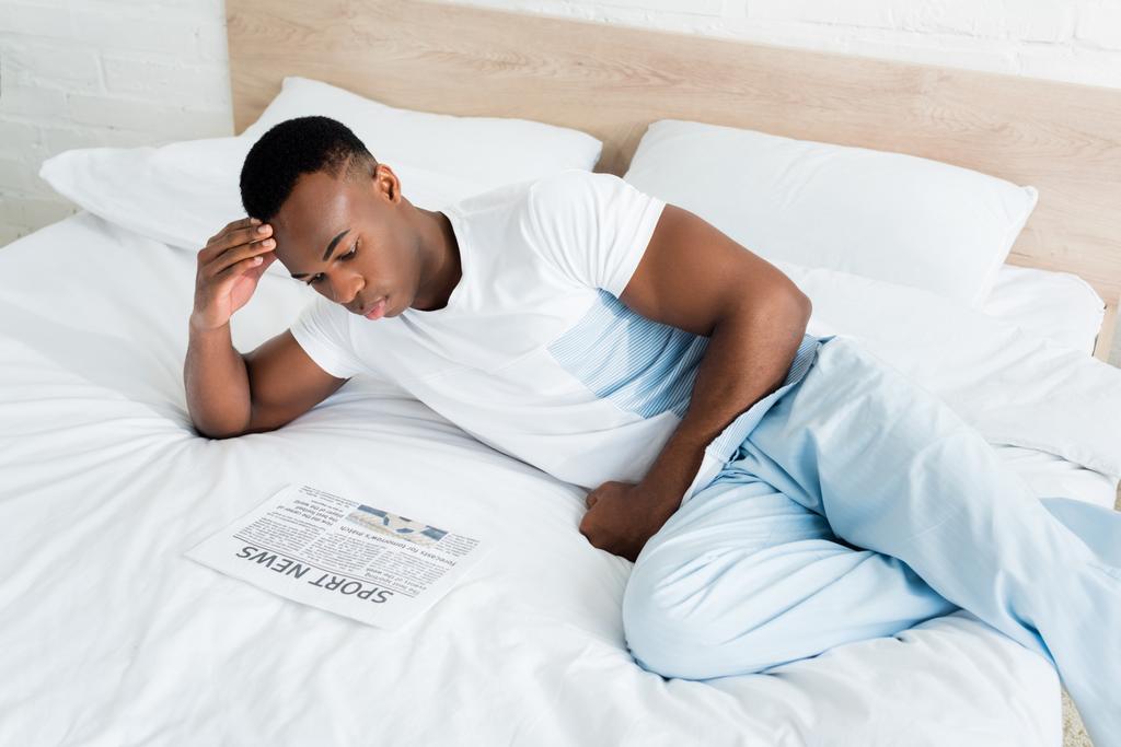 vista de ángulo alto del hombre afroamericano tranquilo leyendo el periódico, acostado en la cama
 - Foto, imagen