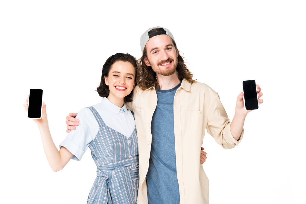 νεαρό ζευγάρι που κρατά smartphones στα χέρια και αγκαλιάζει απομονωμένο σε λευκό - Φωτογραφία, εικόνα