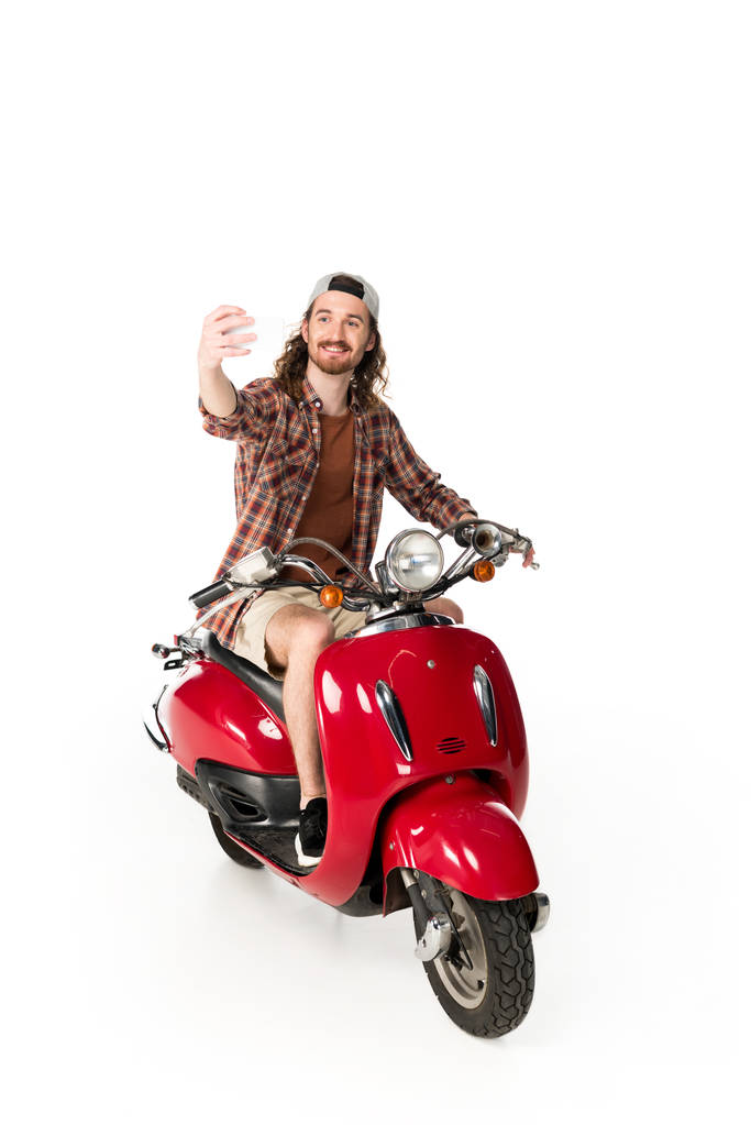 vista completa de hombre joven sentado en scooter rojo y tomando selfie aislado en blanco
 - Foto, Imagen