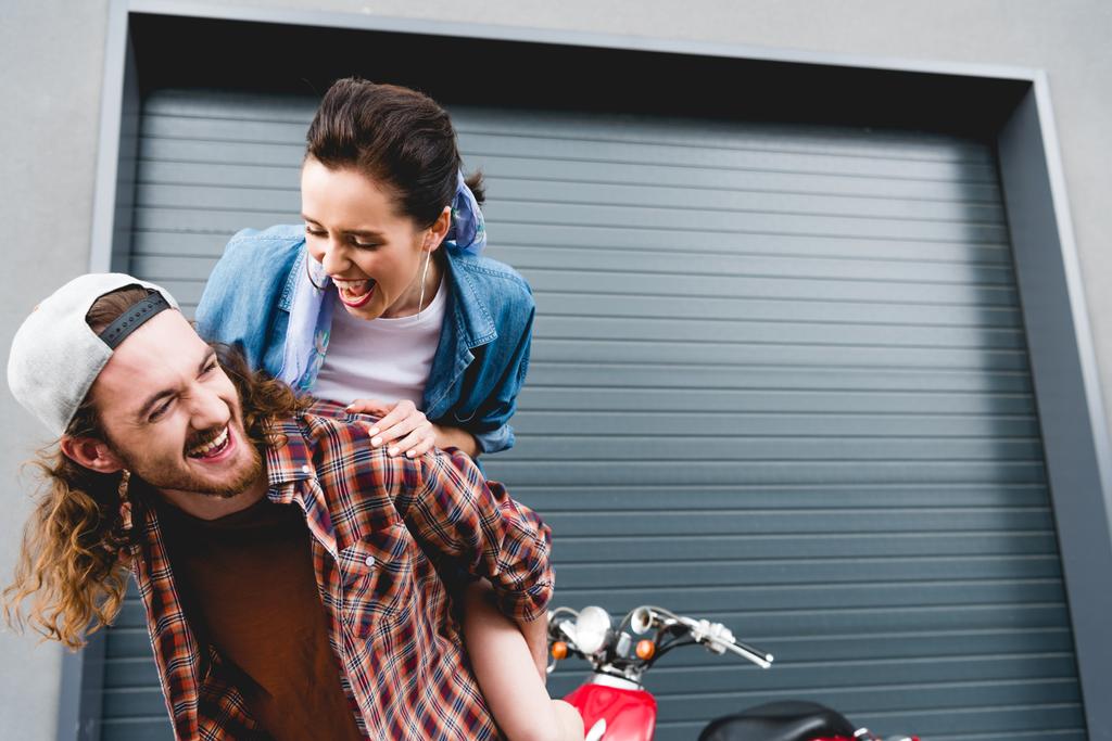 Genç adam ve kız gülüyor, kırmızı scooter 'ın yanında dikilirken sırtına biniyor.  - Fotoğraf, Görsel