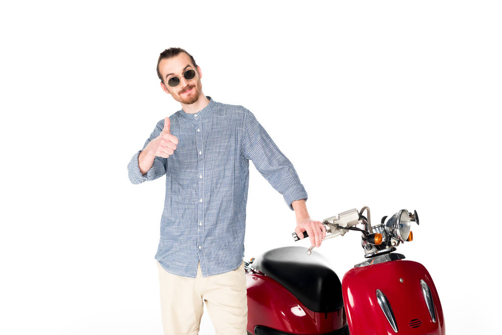 красивый стильный молодой человек стоит рядом с красным скутером, смотрит в камеру и показывает большой палец, изолированный на белом
 - Фото, изображение