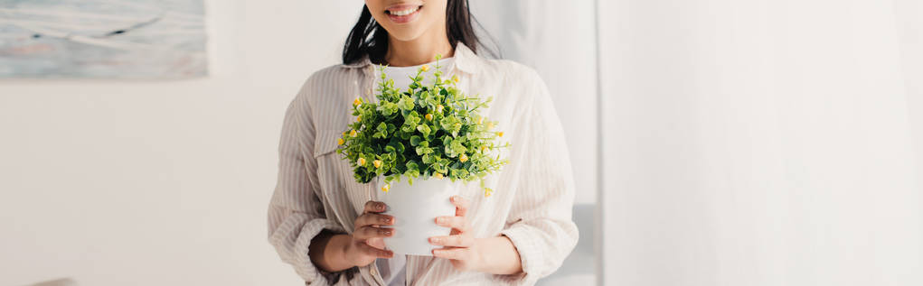 plan panoramique d'une femme latine tenant un pot de fleurs avec une plante verte
  - Photo, image