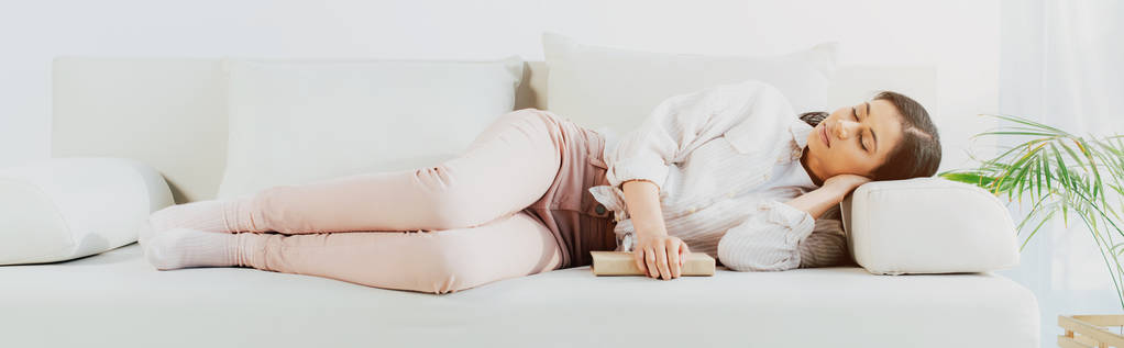 panoramiczny strzał pięknej Łacińskiej kobiety spanie z książki na kanapie w domu - Zdjęcie, obraz