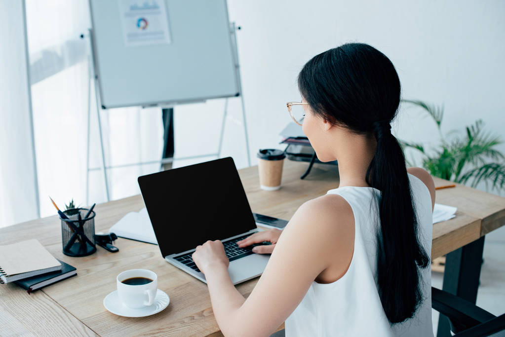 młoda latynoska bizneswoman za pomocą laptopa podczas siedzenia w miejscu pracy w pobliżu filiżanki kawy - Zdjęcie, obraz