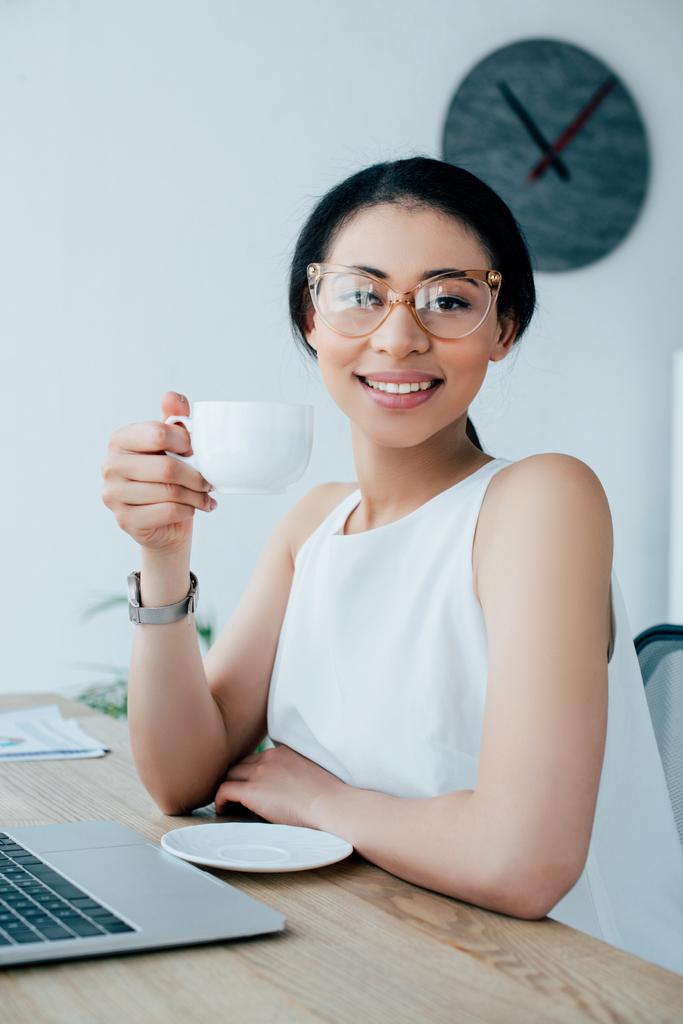 alegre latina empresária segurando xícara de café enquanto sorrindo para a câmera
  - Foto, Imagem