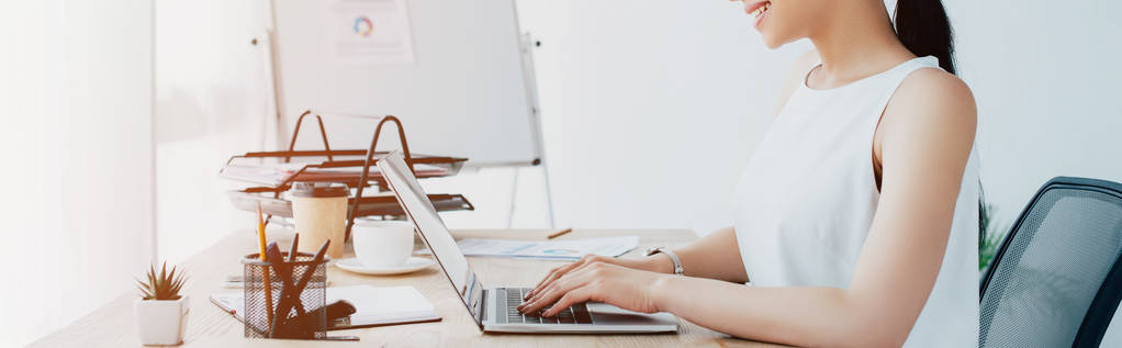 панорамний знімок усміхненої латинської бізнес-леді, що використовує ноутбук на робочому місці
  - Фото, зображення