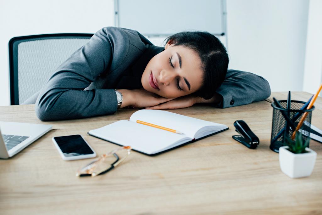 esausta donna d'affari latina che dorme sul posto di lavoro vicino al notebook e allo smartphone con schermo bianco
 - Foto, immagini
