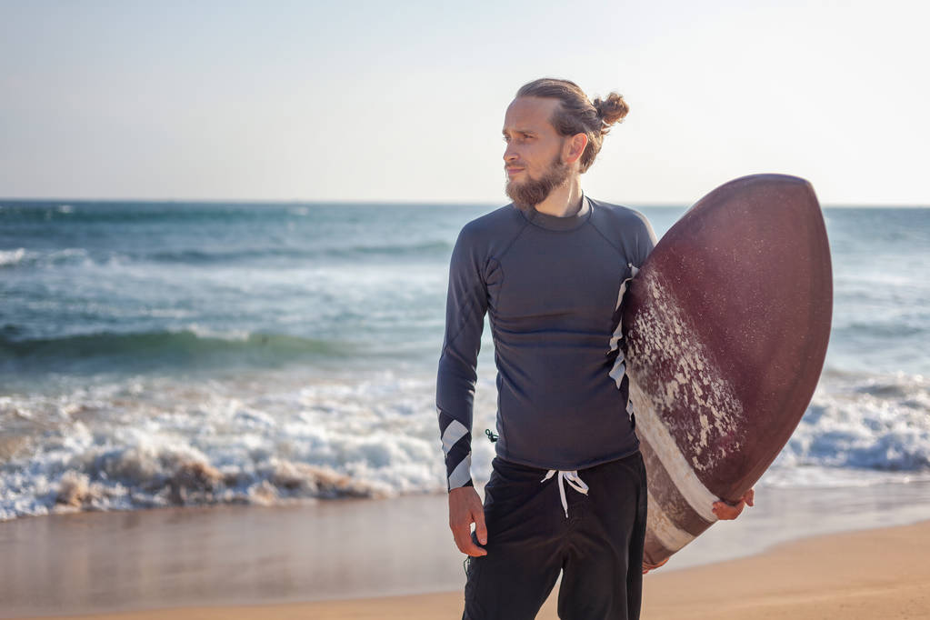 Jovem atraente desportivo elegante homem com uma prancha de surf nas mãos contra o fundo do oceano
 - Foto, Imagem