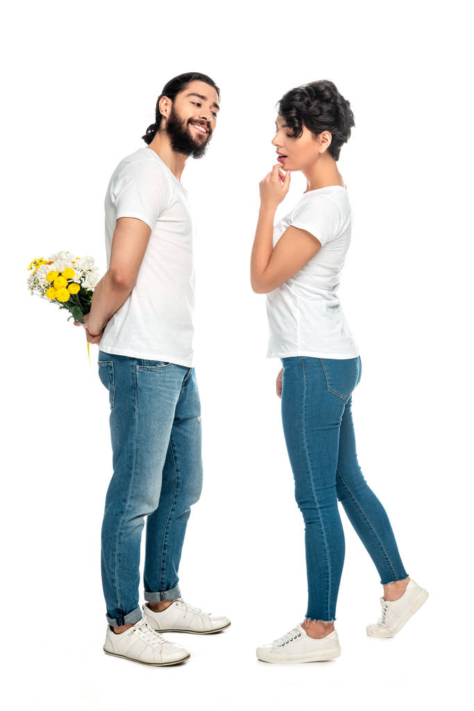 白に隔離された花を持つ陽気なラテンの男の近くに立っている魅力的な女性  - 写真・画像