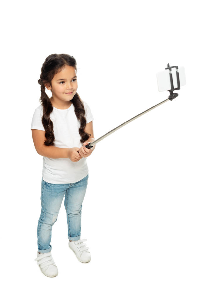 Overhead-Ansicht von glücklichen lateinischen Kind hält Selfie-Stick, während Selfie isoliert auf weiß  - Foto, Bild