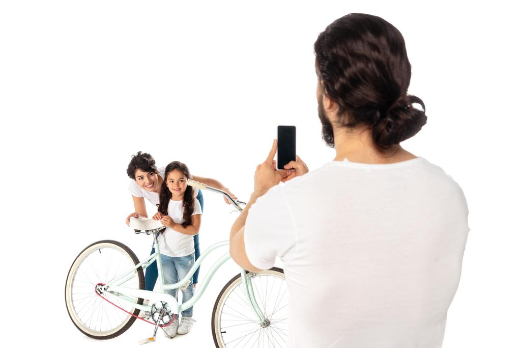 vista posteriore di uomo scattare foto di donna latina e figlia vicino bicicletta isolato su bianco
  - Foto, immagini