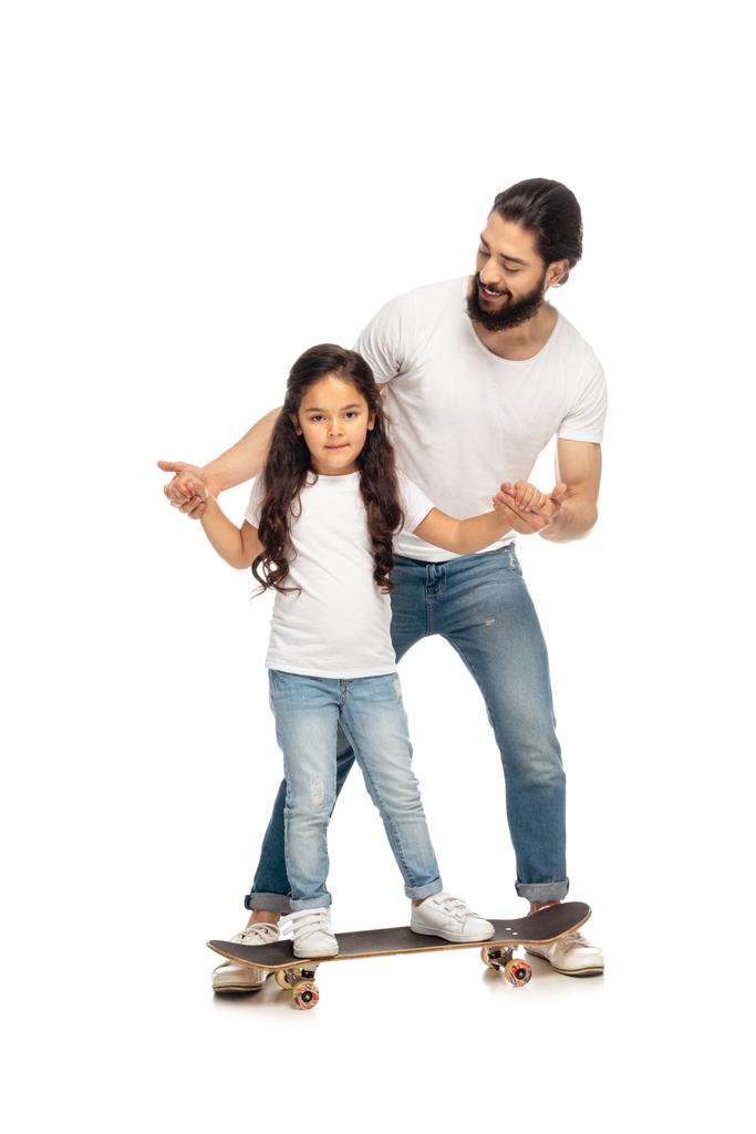 happy latin father holding hands with cute daughter riding penny board isolated on white  - Photo, Image