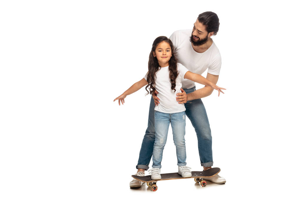 happy latin father looking at cute daughter riding penny board isolated on white  - Photo, Image