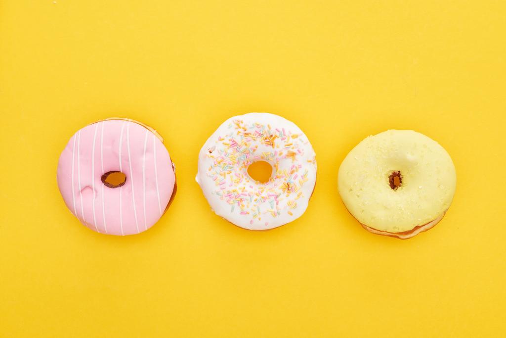 vista superior de saborosos donuts vidrados coloridos no fundo amarelo brilhante
 - Foto, Imagem