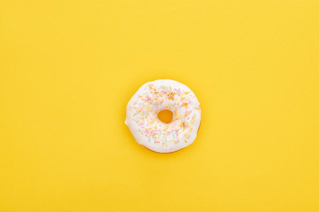 top view of tasty white glazed doughnut with sprinkles on bright yellow background - Photo, Image