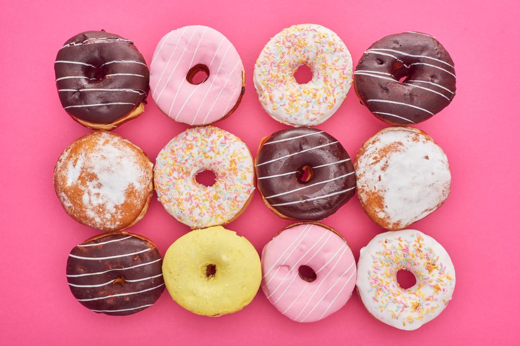 вид сверху на вкусные круглые глазированные пончики на ярко-розовом фоне
 - Фото, изображение