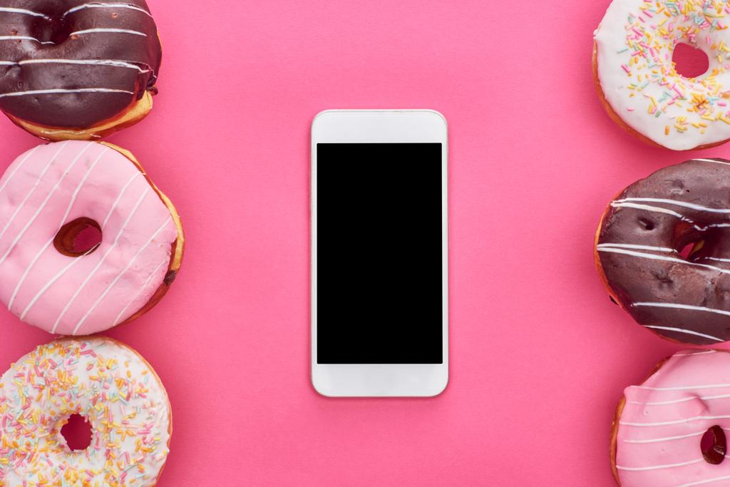 ylhäältä näkymä maukkaita lasitettuja donitseja ja älypuhelin tyhjä näyttö kirkkaan vaaleanpunainen tausta
 - Valokuva, kuva