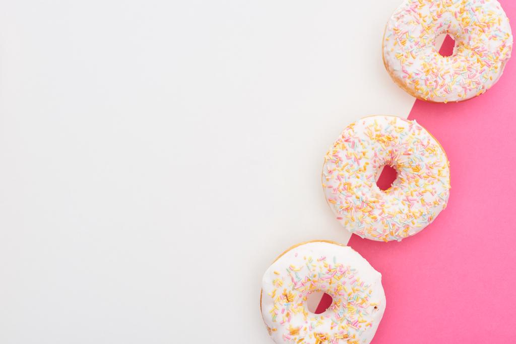 Draufsicht auf leckere glasierte Donuts auf weißem und rosa Hintergrund - Foto, Bild
