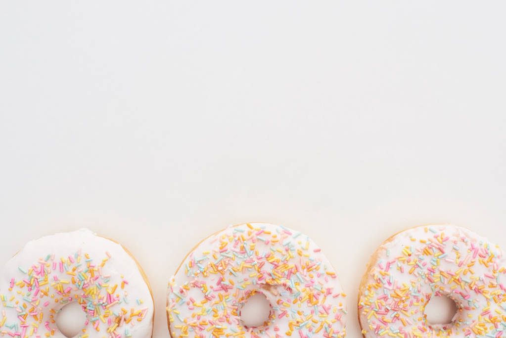 вид сверху на белые пончики с глазурью и брызгами на белом фоне
 - Фото, изображение