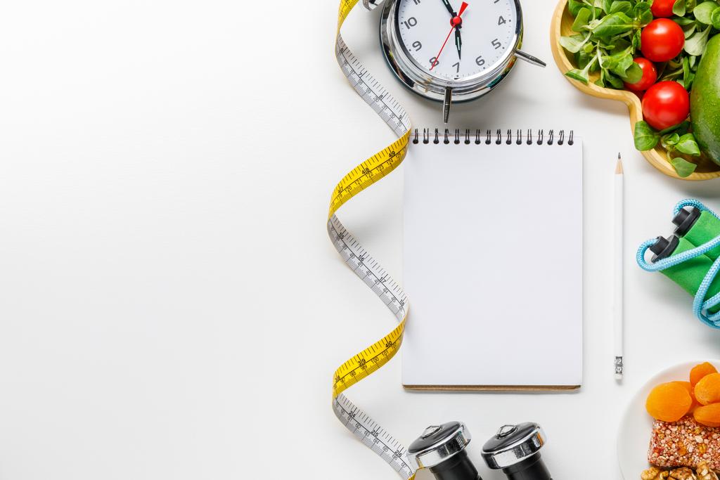 top view of sport equipment, measuring tape, alarm clock and diet food near empty notebook on white background - Photo, Image