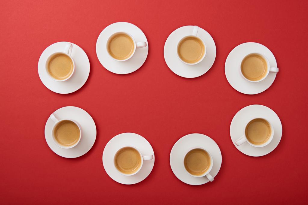 vista dall'alto di tazze bianche con gustoso caffè su piattini su sfondo rosso
 - Foto, immagini