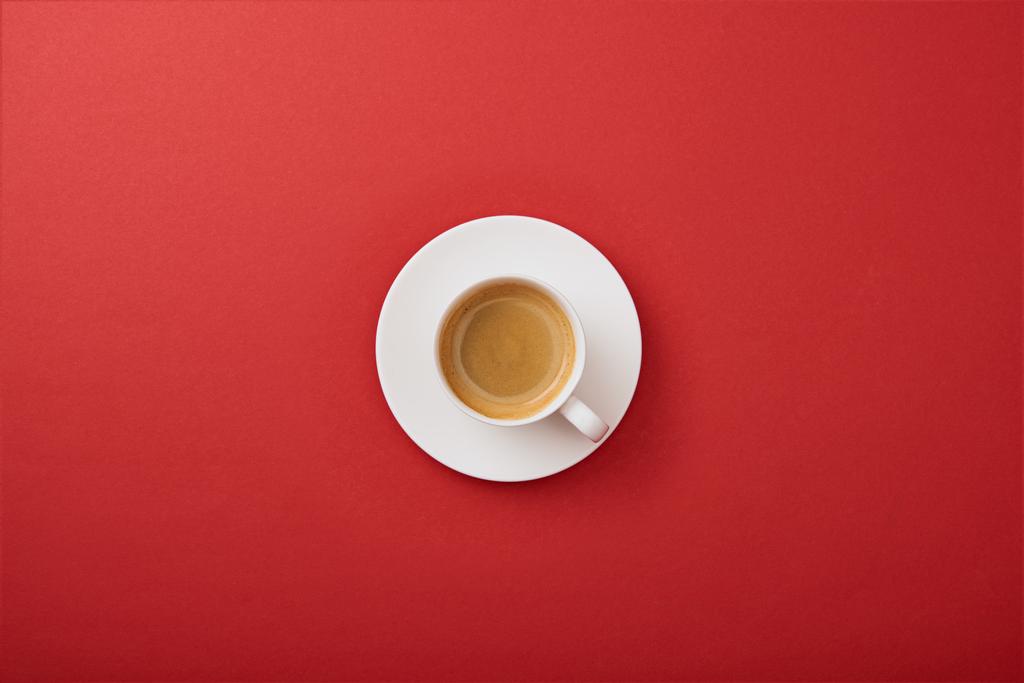 赤い背景にソーサーにコーヒーと白いカップのトップビュー - 写真・画像