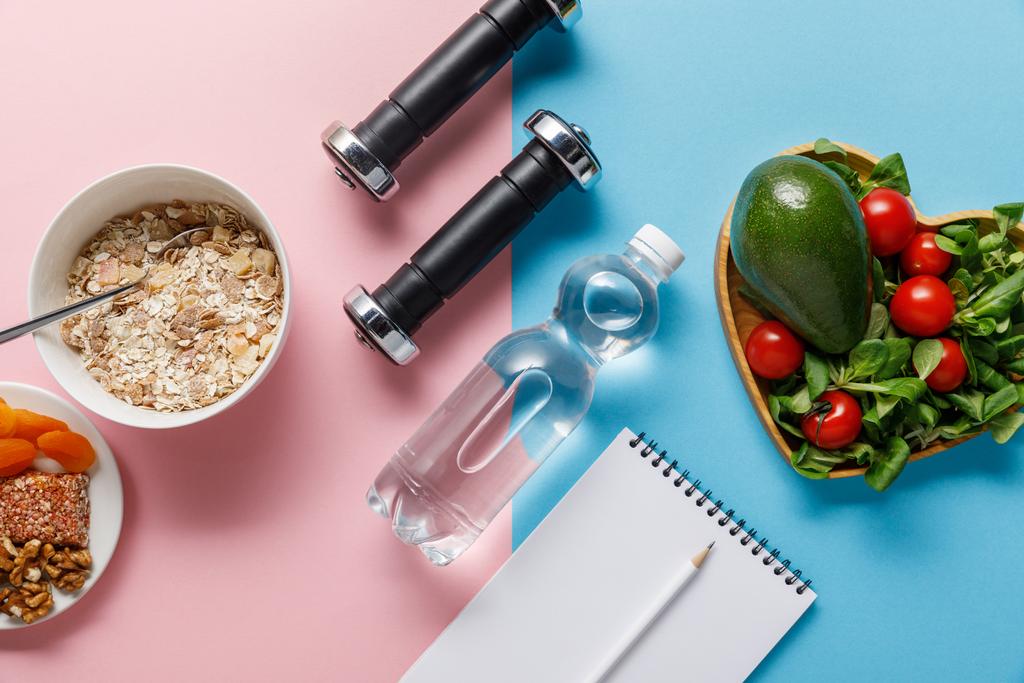 青とピンクの背景にダイエット食品の近くに水、ダンベルと空白のノートブックとボトルのトップビュー - 写真・画像