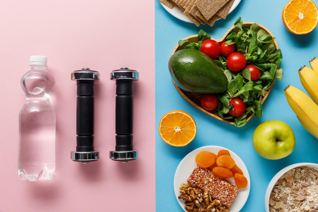 青とピンクの背景にダンベルと水の近くのダイエット食品のトップビュー  - 写真・画像