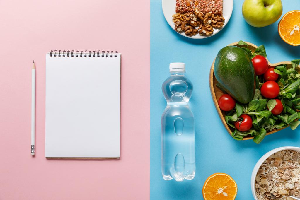 Draufsicht auf Flasche mit Wasser und Diätfutter in der Nähe leeres Notizbuch auf blauem und rosa Hintergrund - Foto, Bild