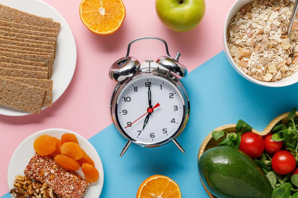 vista superior del reloj despertador de plata con sabrosa comida dietética sobre fondo azul y rosa
  - Foto, Imagen