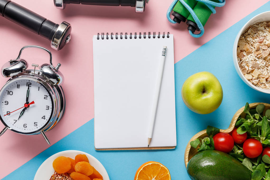 top view of empty notebook and pencil with delicious diet food and sport equipment on blue and pink background  - Photo, Image