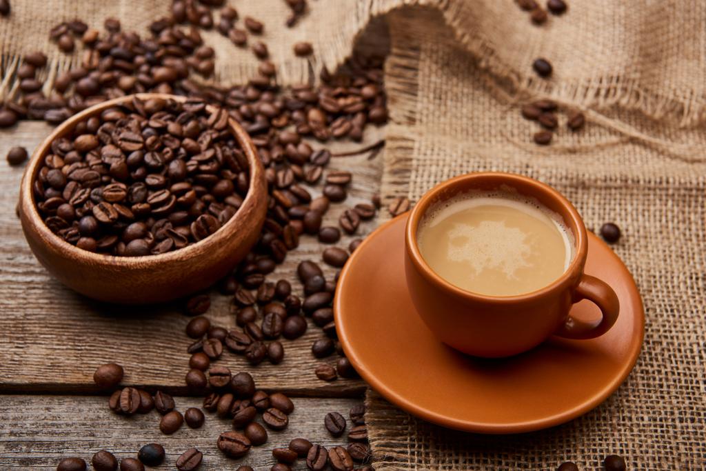 grãos de café na tigela perto de xícara de café em fundo de madeira
 - Foto, Imagem