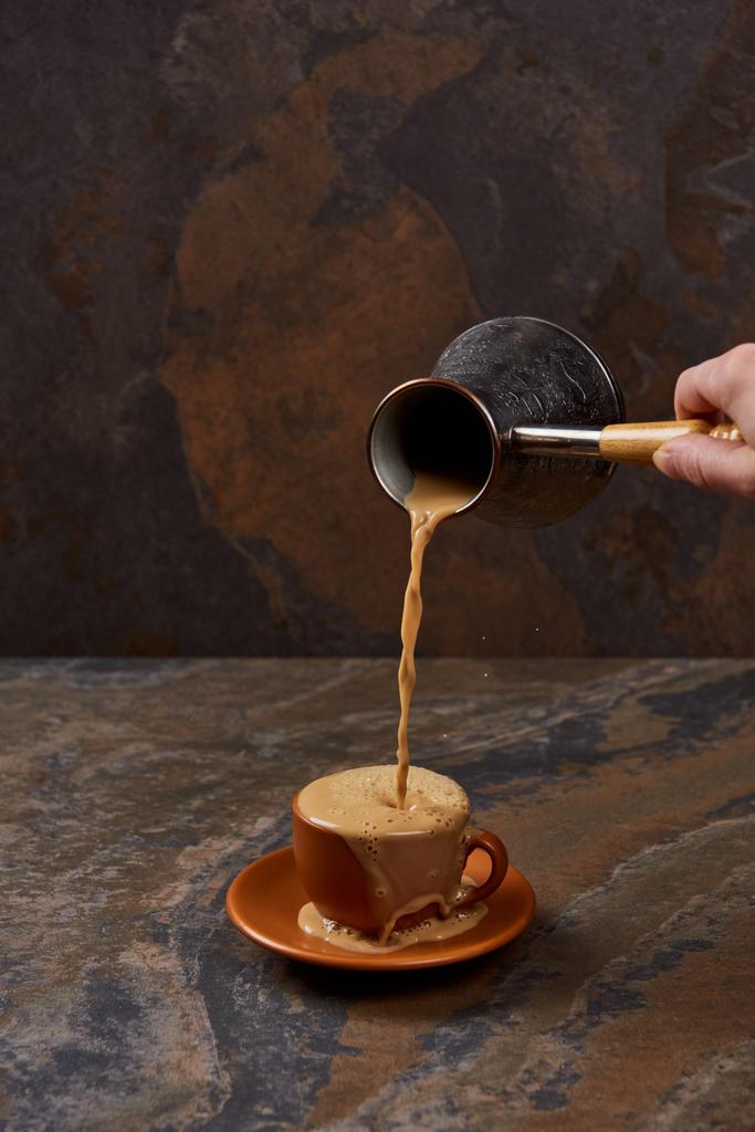 μερική θέα του ανθρώπου που ρίχνει καφέ από μπρίκι σε Κύπελλο σε μαρμάρινη επιφάνεια - Φωτογραφία, εικόνα