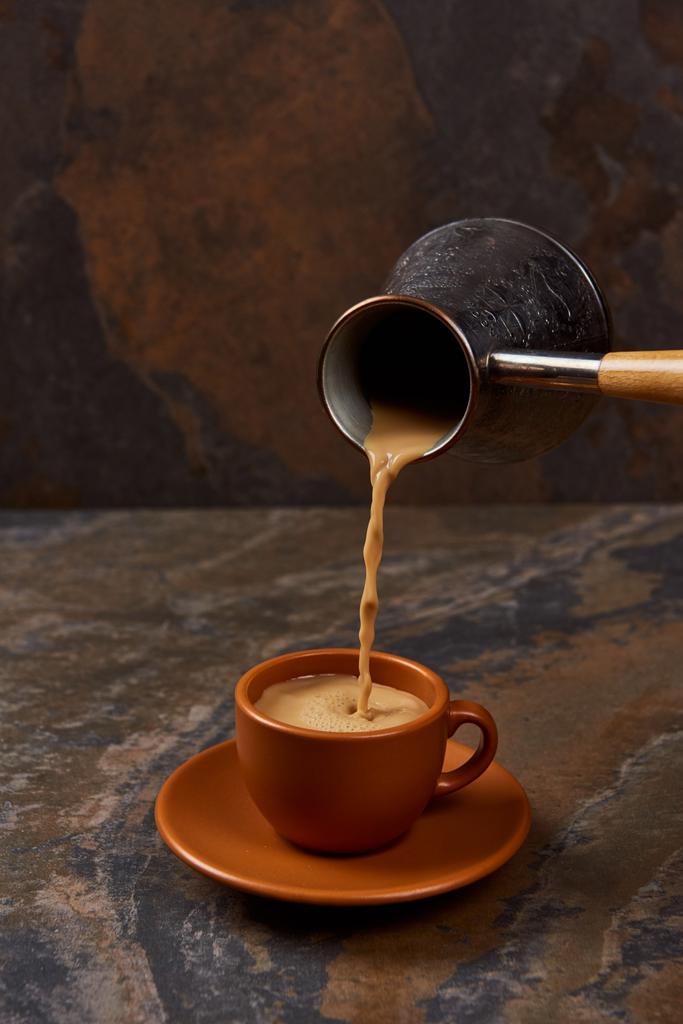 pouring coffee from cezve into cup on saucer on marble surface - Photo, Image