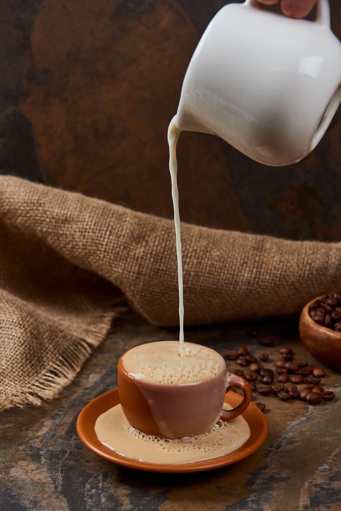 vue recadrée de la personne versant du lait dans une tasse avec café sur une table en marbre près du sac
 - Photo, image