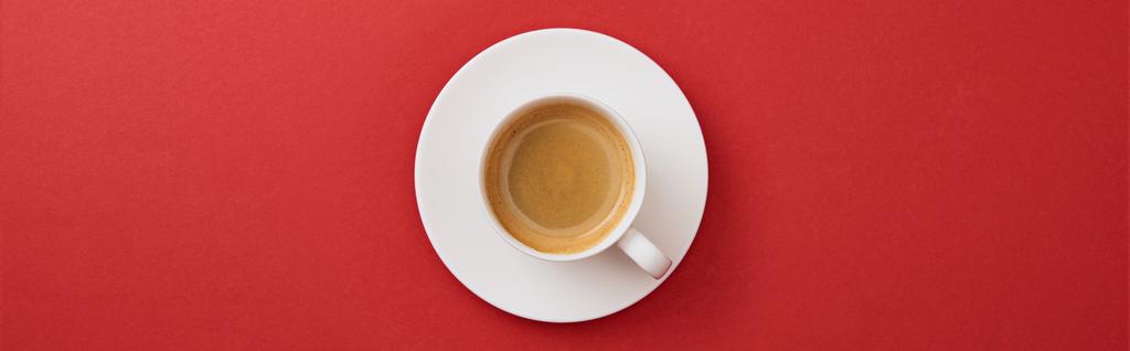 Κορυφαία θέα του λευκού Κυπέλλου με καφέ σε πιατάκι σε κόκκινο φόντο, πανοραμική βολή  - Φωτογραφία, εικόνα