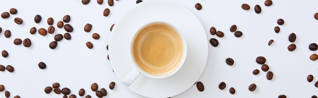白い背景に散らばった焙煎豆の近くにカップでおいしいコーヒーのパノラマショット - 写真・画像