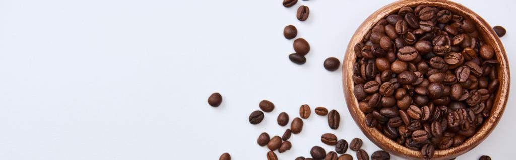 plano panorámico de sabrosos granos de café tostados en tazón de madera sobre fondo blanco con espacio de copia
 - Foto, imagen