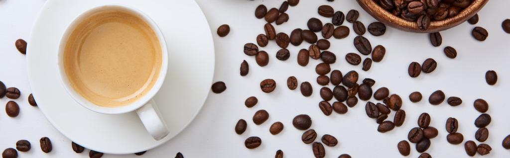 vista superior del café en taza en platillo cerca de granos tostados dispersos, plano panorámico
 - Foto, imagen