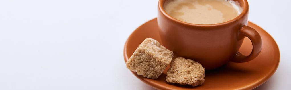 plano panorámico de sabroso café con espuma en taza en platillo cerca de azúcar morena sobre fondo blanco con espacio de copia
 - Foto, Imagen