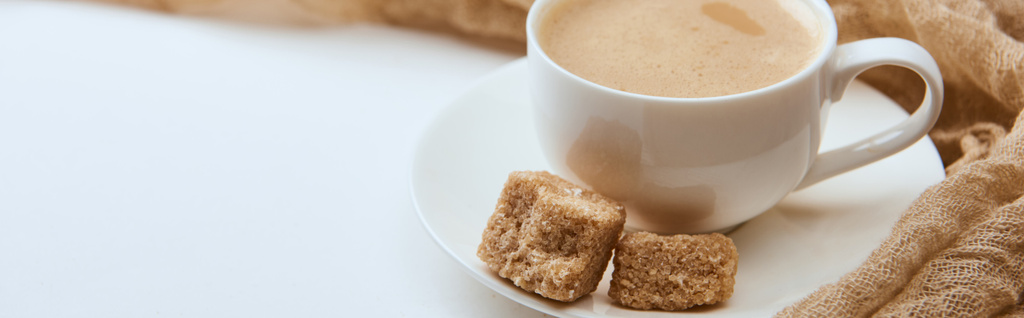 Panoramaaufnahme von leckerem Kaffee mit Schaum in Tasse mit braunem Zucker auf weißem Hintergrund mit Tuch - Foto, Bild